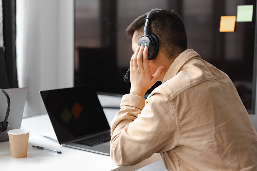 A man wearing headphones works at a laptop in a modern office setting.